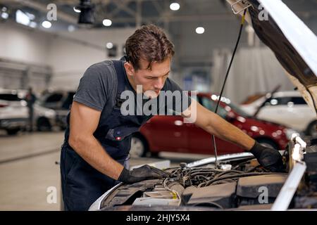 Junge fokussierten amerikanischen oder kaukasischen Mann kann alles beheben. Handsome Automechaniker in der Gesamtuniform Überprüfung des Motors unter der Haube in modernen sauberen Auto Stockfoto