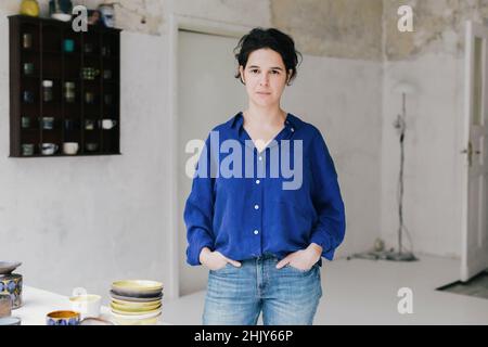 Porträt der Handwerkerin mit Händen in Taschen stehen in Keramik-Shop Stockfoto