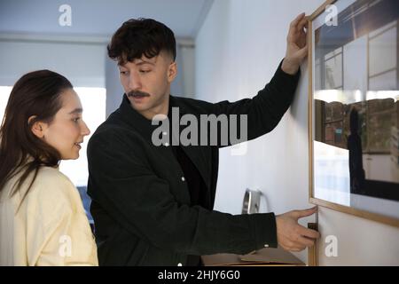 Mann diskutiert mit Freundin, während Bilderrahmen an der Wand im Wohnzimmer hängen Stockfoto