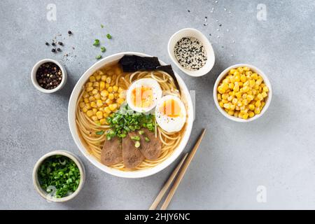 Ramen-Nudeln-Schüssel mit Ei und Fleisch auf grauem Beton-Tischhintergrund, Draufsicht. Asiatische Küche Stockfoto