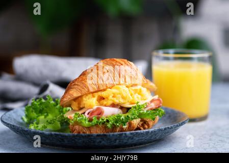 Croissant-Sandwich Mit Schinken, Käse Und Rührei Serviert Mit Einem Glas Orangensaft. Frühstück Oder Mittagessen Stockfoto