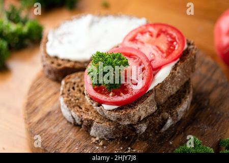 Roggenbrot Toast mit weichem Weißkäse Ricotta und frischer Tomate auf einem hölzernen Schneidebrett. Nahaufnahme Stockfoto