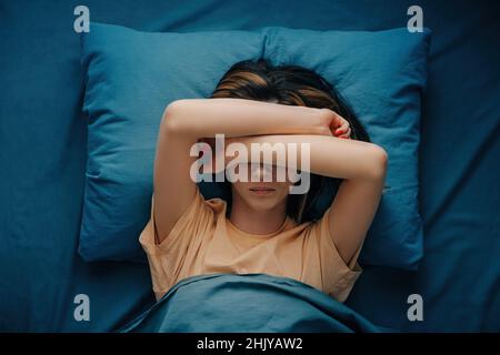 Eine Frau mit Kopfschmerzen oder Migräne liegt im Bett. Stockfoto