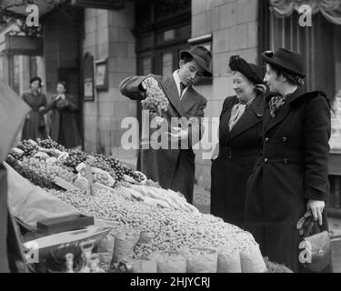 LONDON: Ein Barrow-Junge verkauft in den 1940er Jahren an zwei Frauen mittleren Alters einen Traubenstrauch von seinem Obst- und Gemüsestände am Londoner Strand. Quelle: The DL Archive Collection/Alamy Stockfoto