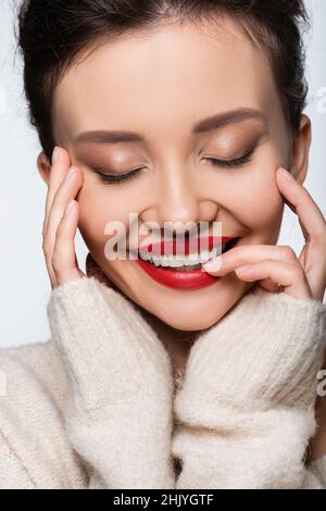 Porträt einer lächelnden Frau im Pullover, die rote Lippen berührt, isoliert auf Weiß Stockfoto