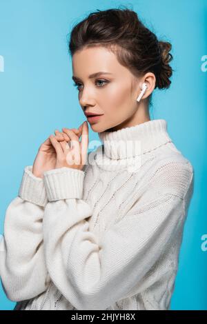 Junge Frau in Strickpullover mit Kopfhörer isoliert auf blau Stockfoto