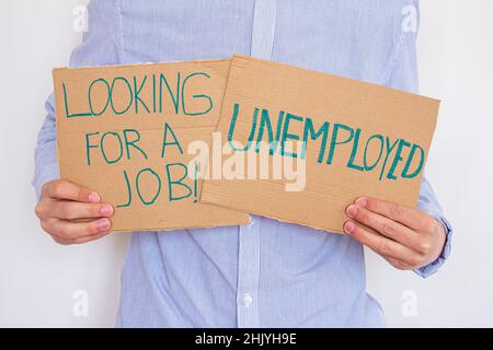 Arbeitsloser Mann mit Schilder mit Aufschrift AUF DER SUCHE NACH Einem JOB. Konzept des Arbeitsplatzverlustes und der Suche nach einem neuen. Er hat finanzielle Probleme. Stockfoto