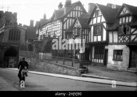 1940s, historische Ansicht aus dieser Zeit des Lord Leycester's Hospital, Warwick, England, Großbritannien. Robert Dudley, Earl of Leicester, der sich neben dem West Gate an der High Street befindet, erwarb die Gebäude im Jahr 1571, um als Krankenhaus für veraltete oder verletzte Soldaten gemäß einer königlichen Charta von Queen Elizabeth 1 verwendet zu werden. In dieser Zeit bedeutete ein Krankenhaus nicht eine medizinische Einrichtung, sondern eher ein Pflege- oder Erholungsheim. Auf der Straße sehen wir einen Mann auf einem Fahrrad, mit einem kleinen Kind, das auf dem Rücken sitzt. Stockfoto