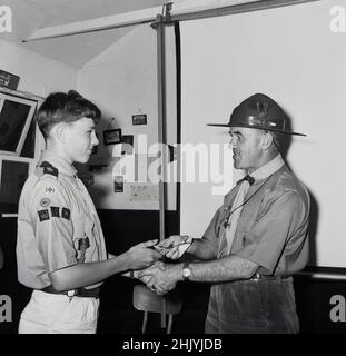 1960s, historisch, 'Well done lad'......inside eine Pfadfinderhalle, ein Pfadfinder, der von einem Pfadfindermeister, Buckinghamshire, England, Großbritannien, mit seinen Abzeichen überreicht wurde. Robert Baden-Powell, ein britischer Kavallerieoffizier, gründete 1908 die Boy Scouts, nachdem er mit seinem Buch Scouting for Boys erfolgreich war. Stockfoto