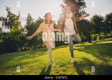 In voller Länge Foto von lustigen alten grauen Haaren Paar laufen tragen lässige Hemden Jeans Schuhe außerhalb Geburtstag im Park Stockfoto