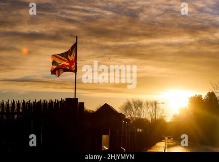 Die Sonne geht über dem Osten von Belfast auf, während die Union Flag im Wind flattert. Stockfoto