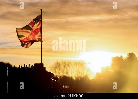 Die Sonne geht über dem Osten von Belfast auf, während die Union Flag im Wind flattert. Stockfoto