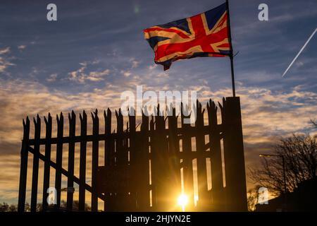 Die Sonne geht über dem Osten von Belfast auf, während die Union Flag im Wind flattert. Stockfoto