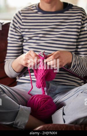 Nahaufnahme Einer Frau, Die Zu Hause Auf Dem Sofa Sitzt, Strickpullover Mit Rosa Wolle Stockfoto