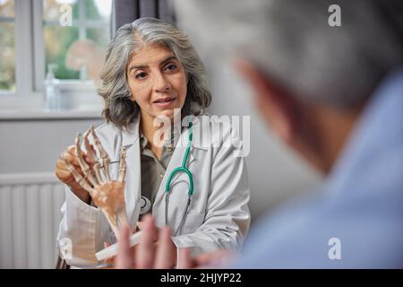 Reife Weibliche Arzt Treffen Mit Männlichen Patienten Diskussion Gelenkschmerzen In Der Hand Mit Anatomischen Modell Stockfoto