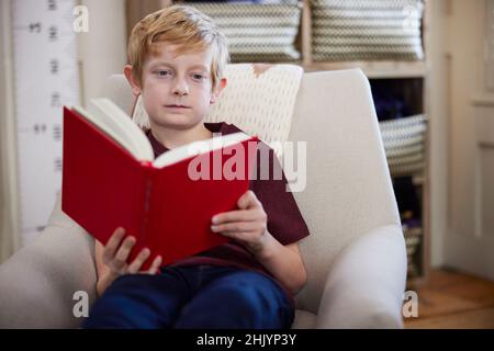 Junge Sitzt Im Stuhl Im Schlafzimmer Zu Hause Lesebuch Stockfoto
