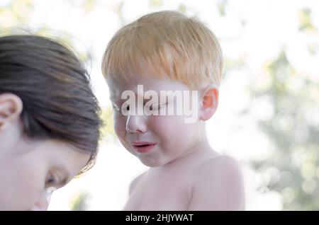 Ein 4-jähriger Junge weint, während seine Mutter einen Splitter herauszieht. Rotschopf kleiner Junge weinend Stockfoto