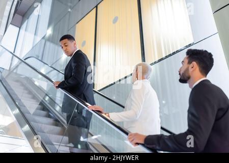 Sicherheitsmänner mit gemischter Kleidung, die eine ältere Geschäftsfrau auf der Hoteltreppe begleiten Stockfoto