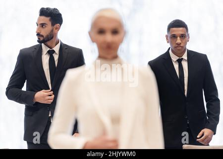 Gemischtrassige Bodyguards in formeller Kleidung begleiten verschwommene Geschäftsfrau während der Geschäftsreise Stockfoto