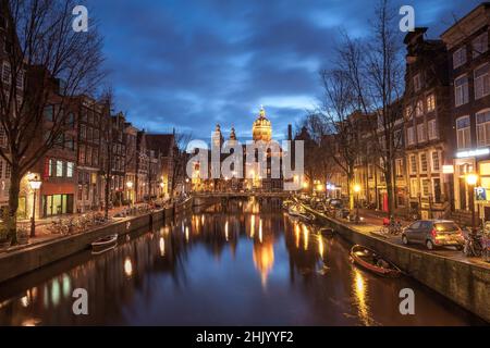 St. Nicolas Kirche und Brücke mit Blick auf einen Amsterdamer Kanal bei Sonnenaufgang mit Kanalbooten und Fahrrädern Amsterdam Holland Stockfoto