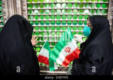 Teheran, Teheran, Iran. 1st. Februar 2022. Eine verschleierte Frau, die eine Schutzmaske trägt, hält eine iranische Flagge, während sie neben dem Grab des verstorbenen iranischen Führers Ayatollah Ruhollah Khomeini am ersten Tag des Sieges des Jahrestages der Islamischen Revolution auf dem Friedhof Behesht-e Zahra im Süden Teherans betet (Foto: © Sobhan Farajvan/Pacific Press über ZUMA Press Wire) Stockfoto