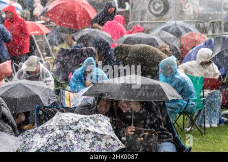 Fans bei einem großen Musikfestival in einem Park in Essex bei starkem Regen. Unter Regenschirmen und Wasserabzeichen gedrängt Stockfoto