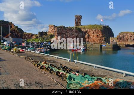 Blick nach Westen über Dunbar Harbour zu den alten historischen Burgruinen. Schöner klarer Tag. Bunte Fischerboote. East Lothian, Schottland, Großbritannien Stockfoto