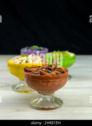 Smoothie oder Pudding mit Schokolade, Haselnüssen und Mandeln zum Frühstück in einer Schüssel mit mehreren anderen Smoothies im Hintergrund serviert Stockfoto