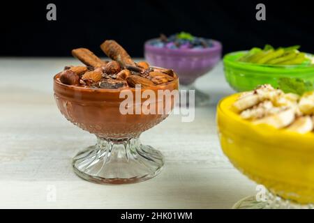 Smoothie oder Pudding mit Schokolade, Haselnüssen und Mandeln zum Frühstück in einer Schüssel mit mehreren anderen Smoothies im Hintergrund serviert Stockfoto