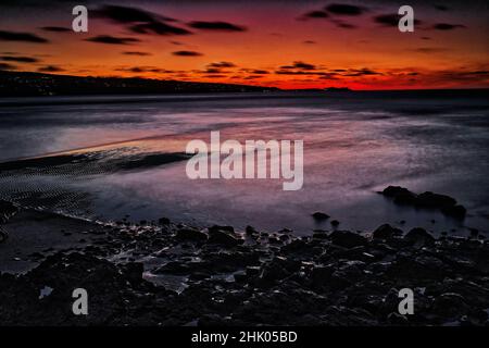 Sonnenuntergang über Strand & Meer mit Felsen im Vordergrund Stockfoto