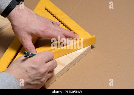 Zimmermann mit einem Bleistift und einem alten Quadrat, das eine diagonale Linie auf einem Holzbrett markiert Stockfoto