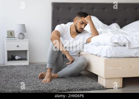 Konzept Für Psychische Erkrankungen. Deprimierter Junger Arabischer Kerl, Der Auf Dem Boden In Der Nähe Des Betts Sitzt Stockfoto