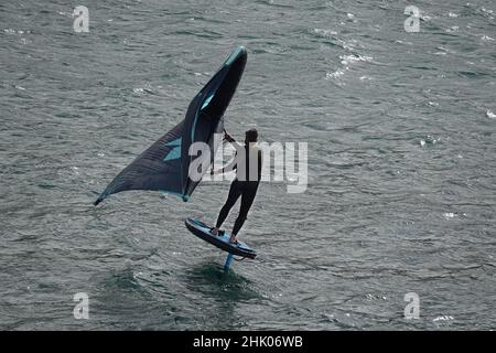 Ein männlicher Surfer, der vor der britischen Küste surft oder mit einem aufblasbaren Flügel flattet Stockfoto