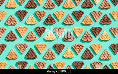 Viele herzförmige Waffeln auf einem grünen Hintergrund ausgerichtet, Blick von oben. Muster mit köstlichen Waffeln aus Kakao, Vanille und Zimt Stockfoto