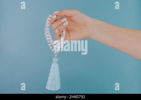 Mondstein mala Perlen in weiblicher Hand auf blauem Hintergrund. Edelsteinstrang, der während der Mantra-Meditationen verwendet wird, um das Zählen zu halten. Spiritualität, Religion, Gott Stockfoto