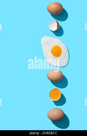 Frische braune Eier, Eigelb und Spiegelei auf blauem Hintergrund mit Copyspace. Vertikales Format. Stockfoto