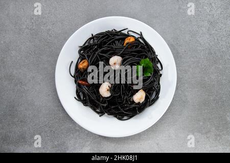 Flache schwarze Pasta mit Meeresfrüchten isoliert auf weißem Teller auf grauem Hintergrund. Draufsicht. Stockfoto