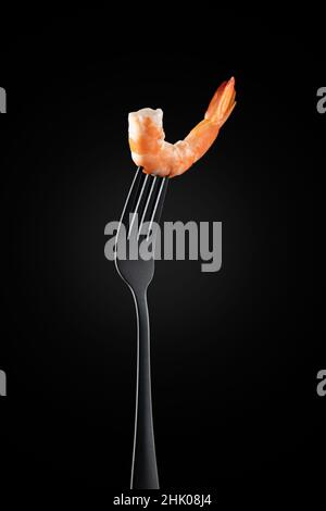 Garnelen auf einer Gabel isoliert. Auf schwarzem Hintergrund. Vertikales Format. Stockfoto