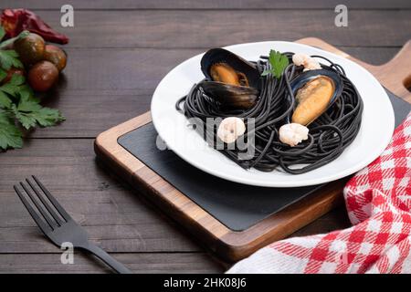 Teller mit schwarzer Pasta mit Meeresfrüchten auf Holzhintergrund. Mediterranes Speisekonzept. Stockfoto