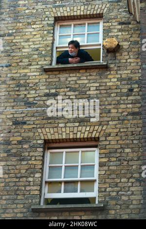 London, Großbritannien. 1. Februar 2022. Ein Mann blickt aus einem Fenster auf den Prinzen von Wales und die Herzogin von Cornwall in Chinatown, um das Mondneujahr, das Jahr des Tigers, mit einem Besuch lokaler Geschäfte, Organisationen und Gemeinden zu feiern. Kredit: Stephen Chung / Alamy Live Nachrichten Stockfoto