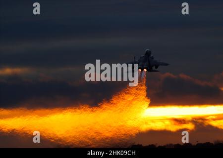 McDonnell Douglas, Boeing F-15E Strike Eagle hebt bei Sonnenuntergang im Nachbrenner ab und erzeugt eine Spur von Hitzedunst, die durch gebrochenes Licht betont wird Stockfoto