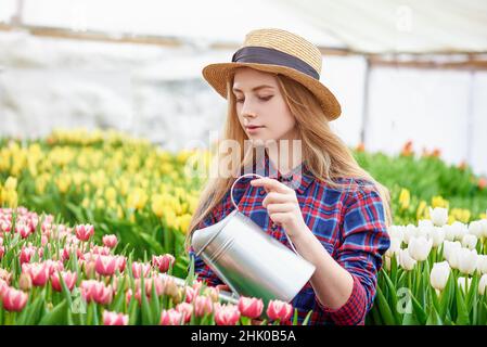 Glücklich lächelnd Teenager Mädchen im Hut mit Gießkanne in Blühender Tulpengarten Stockfoto