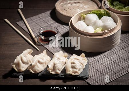 Dim Sum in Bambusdampfer und Gyozas mit Sojasoße auf dunklem Hintergrund. Stockfoto