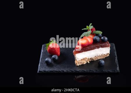 Stück Käsekuchen mit frischen Erdbeeren und Heidelbeeren isoliert serviert auf Schieferteller auf schwarzem Hintergrund mit Copyspace. Hausgemachter Bäckerconcep Stockfoto