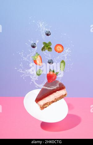 Fliegender Käsekuchen und Erdbeeren mit Heidelbeeren mit Spritzer auf rosa und blauem Hintergrund mit Copyspace. Levitation-Konzept der Bäckerei. Stockfoto