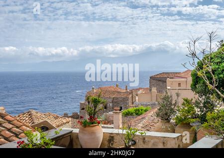 Traditionelle Hausdächer in der mittelalterlichen Burgstadt Monemvasia. Tiefblaues Meer und wolkiger Himmel am Horizont. Panoramablick Stockfoto