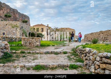 Touristen besuchen die historische Burgstadt auf der Insel Monemvasia, Griechenland. Traditionelle Häuser und mittelalterliche Stadtmauern in einer natürlichen Umgebung Stockfoto