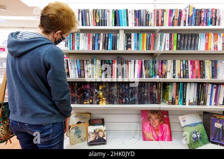 Eine Kundin stöbert in einem lokalen PDSA Charity Shop in der High Street in Großbritannien durch eine Auswahl von Second-Hand-Buchspenden Stockfoto