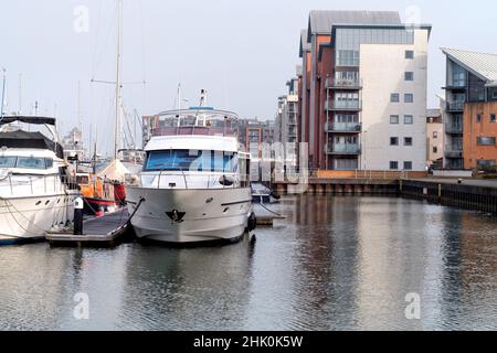 Boote, die in der Portishead Quays Marina nebeneinander aneinandergetäut sind.das Bild zeigt eine teure Yacht, die in der Nähe von angrenzenden Wohnungen und Häusern am Kai festgebunden ist Stockfoto