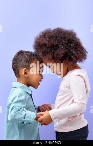 Zwei schöne Kinder Freunde umarmt halten Hände zusammen isoliert über lila Pastellfarben Hintergrund, entzückende Kind Junge und Mädchen in Freizeitkleidung posiert ha Stockfoto